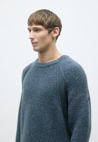 Strickpullover in Dunkelblau mit strukturiertem Oberflächen, ausgestattet mit grünen Seitenteilen und einem Rundhalssausschnitt. Weiches, lässiges Fit-Design.