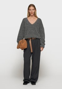 Grauer, übergroßer Wollmischpullover mit V-Ausschnitt, kombiniert mit dunkelgrauen, weiten Hosen und einer braunen Schultertasche mit einem Tragegurt.