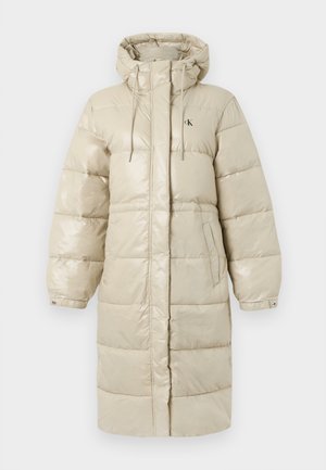 Dlouhý béžový prošívaný kabát s kapucí, šňůrkami, manžetami na cvoky, bočními kapsami a skrytým předním zapínáním na zip, s malým logem „cK“ na hrudi.