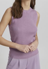 Top sans manches en lilas à côtes avec un col montant et une silhouette ajustée. Ourlet ajusté à la taille. La texture du tissu est lisse et légèrement extensible.
