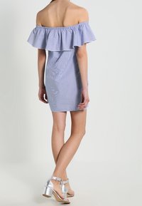 Sukienka na ramiączkach w jasnoniebieskim i białym w paski, z falbaną przy dekolcie. Połączona z srebrnymi sandałami na obcasie.