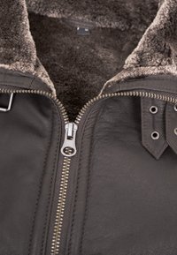 Dunkelbraune Lederjacke mit Schaffellkragen, ausgestattet mit einem silbernen Reißverschluss und Druckknöpfen, strukturiertem Oberflächenmaterial und stabilen Nähdetails.