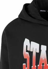 Sudadera negra con una gran impresión en degradado blanco y rojo de la palabra "STARTER" en el pecho. Hecha de suave material de algodón.