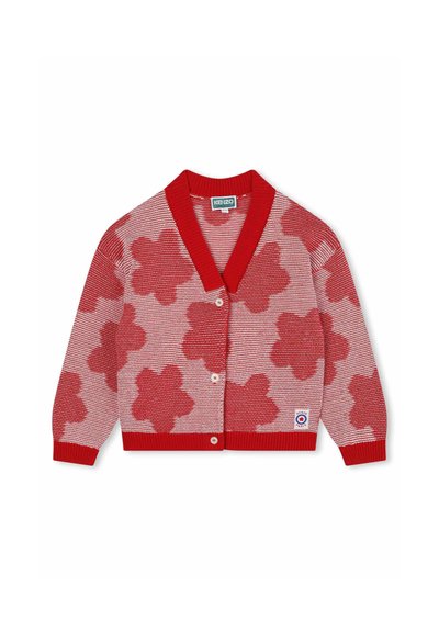 Cardigan en tricot rouge avec un motif de fleurs rouges et blanches, col châle, fermeture par boutons, et poignets et ourlet côtelés. Étiquette visible en bas à droite.