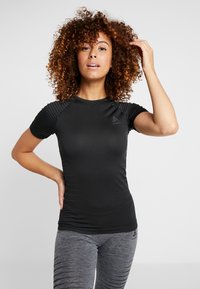 Black short-sleeve athletic shirt with ribbed shoulder texture, paired with grey leggings. Fabric appears smooth and fitted. Logo featured.