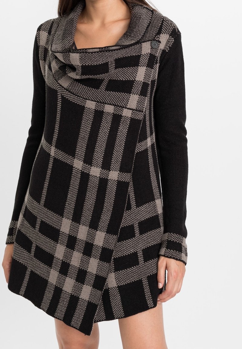 Abito lavorato a maglia con scollatura a barchetta, caratterizzato da un motivo a quadri nero e beige, maniche lunghe e un orlo leggermente asimmetrico.