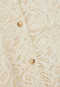 Kantstof in crème met een bloemenpatroon, voorzien van decoratieve knopen. Gelaagd oppervlak en ingewikkelde details overal.
