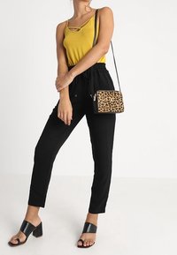 Gul spaghetti-strop top, sorte tilspidsede bukser og sorte hælsandaler. Mønstret håndtaske med leoparddesign. Simpelt og moderne outfit.