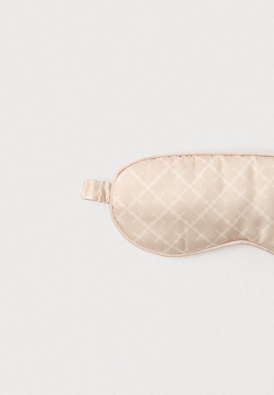 Mască de dormit din satin bej cu textură matlasată, având un model subtil în formă de diamant și o curea laterală pentru fixare sigură.