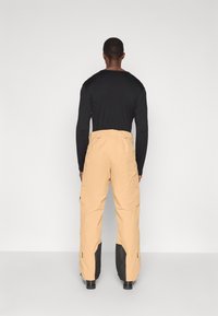 Bež hlače s cargo dizajnom in črnimi detajli, ki imajo ravno nogavico, več žepov in funkcionalen pas. Narejene so iz trpežnega materiala.