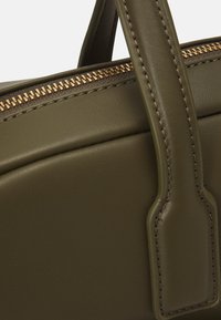 Olivgrüne Ledertasche mit goldfarbenem Reißverschlussdetail, strukturiertem Design, oberen Griffen und sichtbaren Nahtakzenten an der Seite.