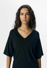 Black V-neck sweater made of soft material with short, wide sleeves and a relaxed fit, featuring a smooth texture without patterns.