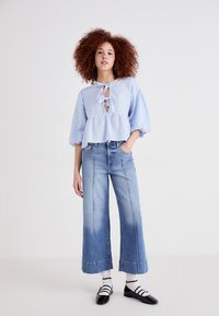 Blusa in gingham azzurro chiaro con fiocco, maniche corte a sbuffo, abbinata a jeans in denim sbiadito a gamba larga e scarpe in vernice nera.