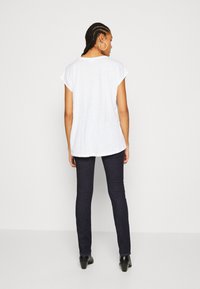 Hvit T-skjorte med korte ermer og rundsaum, kombinert med mørke skinny jeans og ankelstøvler. Enkelt design uten synlige mønstre.