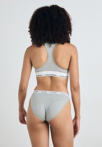 Szürke pamut sportmelltartó széles pántokkal és Calvin Klein logós szalaggal, párosítva a megfelelő, logós díszítésű hipster bugyival.