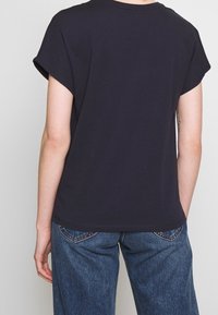 Camiseta negra de algodón de manga corta con un corte relajado, cuello redondo, textura suave y un diseño sencillo, mostrada desde la parte de atrás con jeans azules.