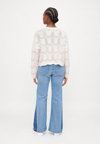 Suéter branco de malha com trama aberta e padrão de riscas em tons pastel, combinado com jeans azuis claros a boca de sino com detalhes em painel lateral.