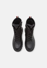 Bottes de cheville en cuir noir avec une finition texturée, bout rond, col rembourré, laçage sur le devant et zippers latéraux avec des accents rouges et blancs.