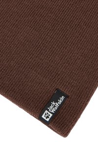 Berretto di maglia marrone con texture a costine. Presenta un'etichetta nera con il logo "Jack Wolfskin". Design semplice adatto per l'abbigliamento outdoor.