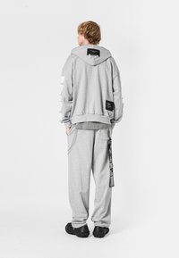 Sudadera gris de gran tamaño con una superficie texturizada, que presenta una etiqueta prominente en la parte posterior, y pantalones jogger a juego. Acentos negros en los pantalones.