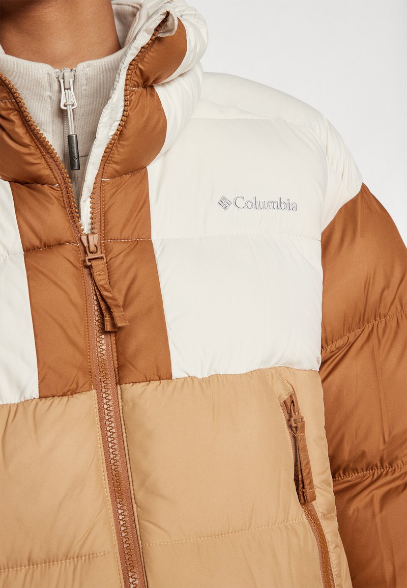 Veste en duvet marron et crème avec des panneaux verticaux. Elle dispose d'une fermeture éclair, d'un col haut et d'un logo sur la poitrine.