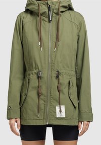Giacca a vento verde oliva con cappuccio, zip frontale, cordini regolabili in vita, tasche con patta e un'etichetta bianca nella parte anteriore bassa.
