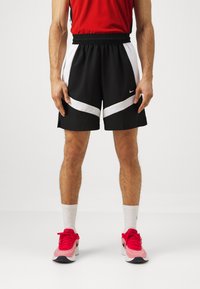 Black athletic shorts with white diagonal accents, elastic waistband, and a small Nike logo on the left side. Worn with red shoes and white socks.