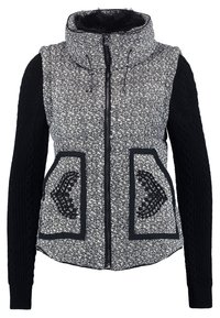 Textureret sort og hvid vest med høj krave, lynlåslukning, to frontlommer og sorte strikkede ærmer. Accentueret med detaljeret syning.