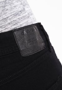 Černé džíny z denimu s texturovanou koženou etiketou na pase, s viditelným šitím a slim fit designem.