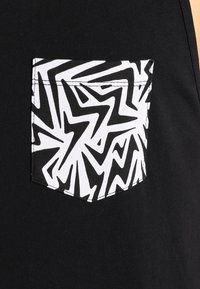 Czarna tkanina z białą kieszenią z odważnymi, abstrakcyjnymi wzorami czarnych zygzaków i kątowych linii.