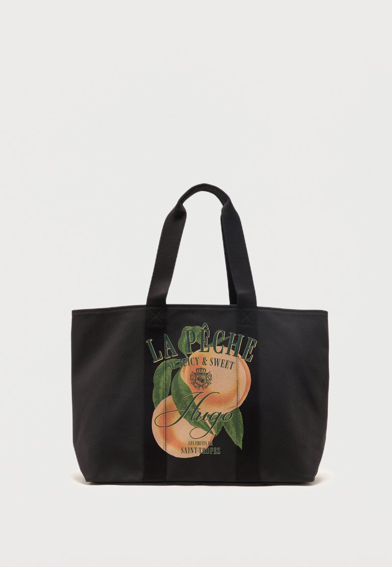 Sac fourre-tout noir avec deux poignées, présentant un graphisme de pêche et le texte "La Pêche Juicy & Sweet Hugo Saint-Tropez" sur le devant.