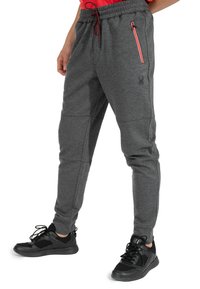 Graue sportliche Jogginghosen mit strukturierter Oberfläche, taillierter Form, elastischem Bund und Seitentasche mit rotem Reißverschlussdetail. Schwarze Sneaker.