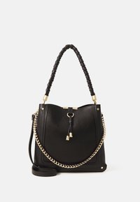 Czarna skórzana torebka o wyraźnej, usztywnionej formie, z plecionym uchwytem u góry, złotym łańcuszkiem dekoracyjnym i zaciąganym zamknięciem. Teksturowane wykończenie z złotymi elementami metalowymi.