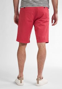 Rode katoenen shorts met rechte snit, twee achterzakken en knoopsluitingen. Draag ze met beige sneakers.