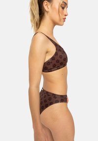 Brun baddräkt med blommönster, bestående av en bralette-topp med tunna axelremmar och högmidjade underdelar, tillverkad av mjukt, elastiskt tyg.