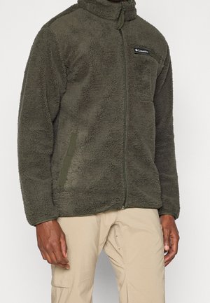 Man draagt een olijfgroene fleecejas met voorrits, borstzak en beige cargobroek.