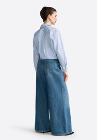 Nieformalna koszula zapinana na guziki w niebiesko-białe paski, w luźnym kroju, zestawiona z szerokimi dżinsami w kolorze niebieskim, z tylnymi kieszeniami i postrzępionymi końcami.