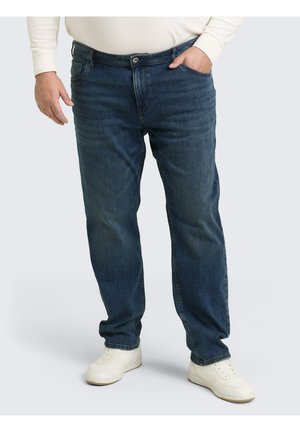 Donkerblauwe denim jeans met rechtlopende pijpen, contrasterende stiksels, voorzakken en een knoopsluiting. Gecombineerd met witte sneakers.