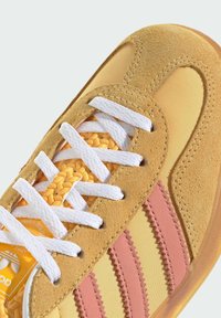 Zapatillas de ante amarillo y malla con cordones blancos, franjas rosas y un detalle texturizado único en la lengüeta. Suela de goma.