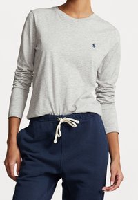 Maglietta a maniche lunghe grigia in tessuto morbido, con colletto rotondo e un piccolo logo blu navy. Abbinata a pantaloni della tuta blu navy scuri con coulisse.