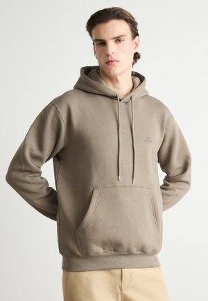 Haut à capuche marron en tissu doux avec une poche avant, des cordons de serrage et un logo subtil sur la poitrine. Coupe décontractée avec une poche kangourou.