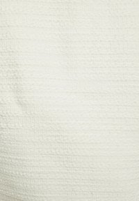 Tessuto bianco testurizzato con un sottile motivo intrecciato. La superficie appare leggermente in rilievo, creando una qualità tattile.