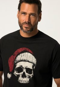 Zwarte katoenen t-shirt met een grote witte schedelafbeelding die een rode santa-hat draagt, met een ronde halslijn en korte mouwen.
