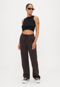 Melnā īsā tanki, brūnas brīvas jogger bikses, sudraba akcenti uz apaviem, ar gludu tekstūru un saite uz jostas.