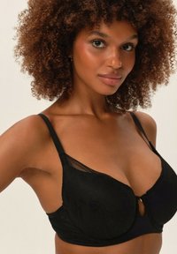 Czarny koronkowy stanik z detalem w kształcie dziurki, wsparciem na drutach i regulowanymi ramiączkami, o gładkim wykończeniu tkaniny.