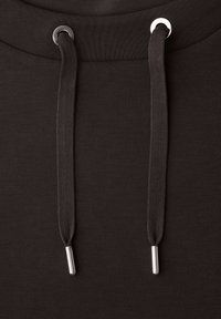 Primer plano de tela de sudadera negra con capucha, con dos cordones negros pasados por ojales plateados.