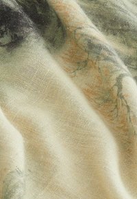 Lätt, strukturerad tyg i krämfärgad och mjuk grön med subtila mönster. Visar naturliga fibrer och variationer i färg och design.