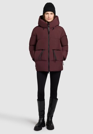 Bordeaux puffer jack met een hoge kraag, voorzijde met rits en twee zwarte horizontale zakken. Draagt met zwarte leggings en hoge laarzen tot de knie.