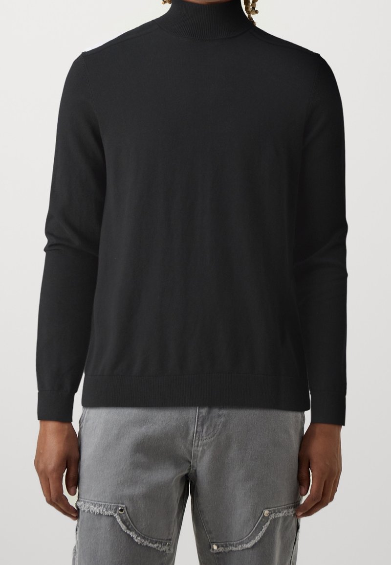 Czarny golf z długimi rękawami, prążkowanym kołnierzem i mankietami, wykonany z miękkiej, gładkiej tkaniny, w połączeniu z szarymi spodniami cargo.