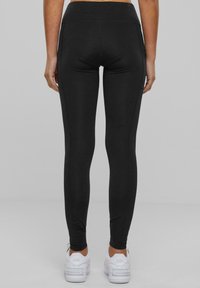 Leggings neri con vita alta, texture liscia e vestibilità snella, abbinati a sneaker sportive bianche.